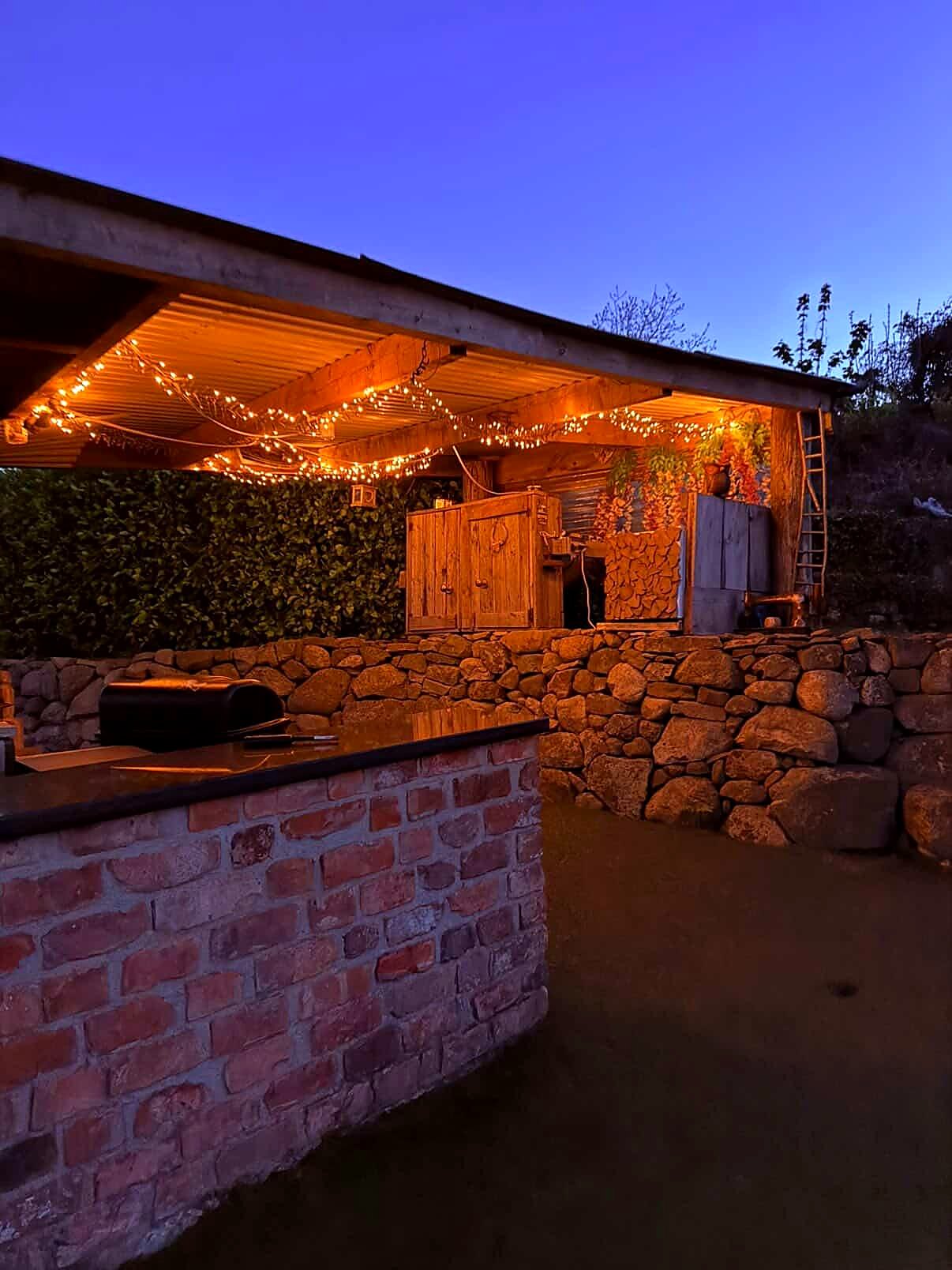 The outdoor kitchen and stone walls lit under a deep blue evening sky