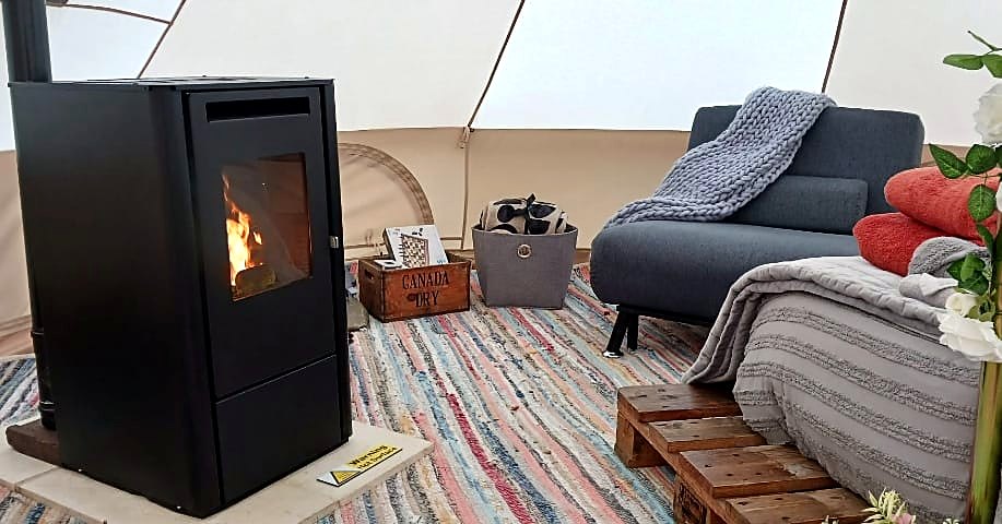 Wood pellet stove burning inside Fairy Fort beside a sofa, rug and made-up bed with towels