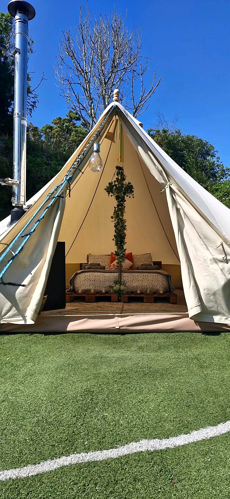 Fairy Cove bell tent open to the lawn on a bright day, its stove flue rising beside the canvas