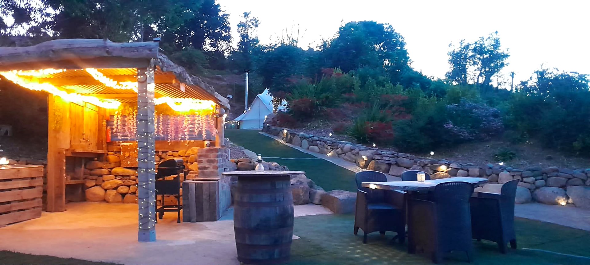 The cooking shelter lit with fairy lights at dusk, table and chairs set outside