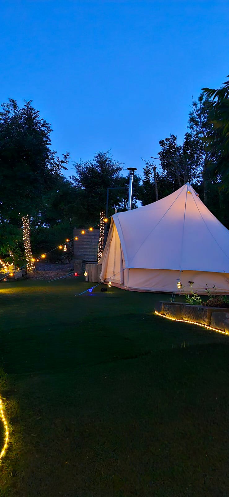 Fairy Fort bell tent lit under a deep blue sky with fairy lights along the lawn and trees