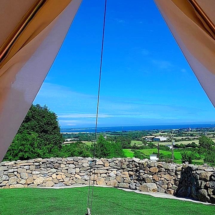 View from inside Fairy Hill through the open canvas door over stone walls and fields to the sea under a blue sky