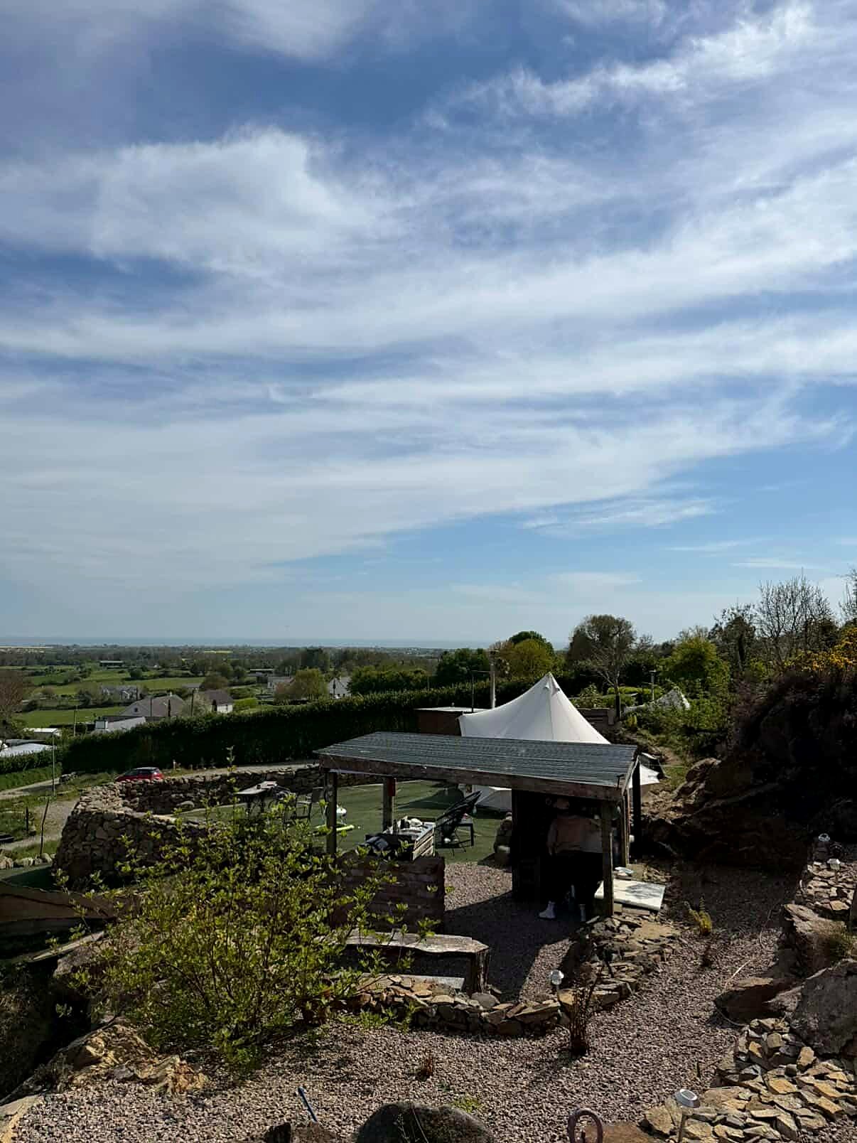 Looking down from Fairy Hill over the stone-walled site and covered shelter towards the fields and the coast